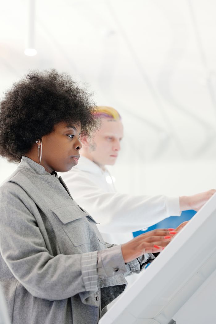 gallery-1 Side view of a fashionable woman with afro hair using a touchscreen indoors.